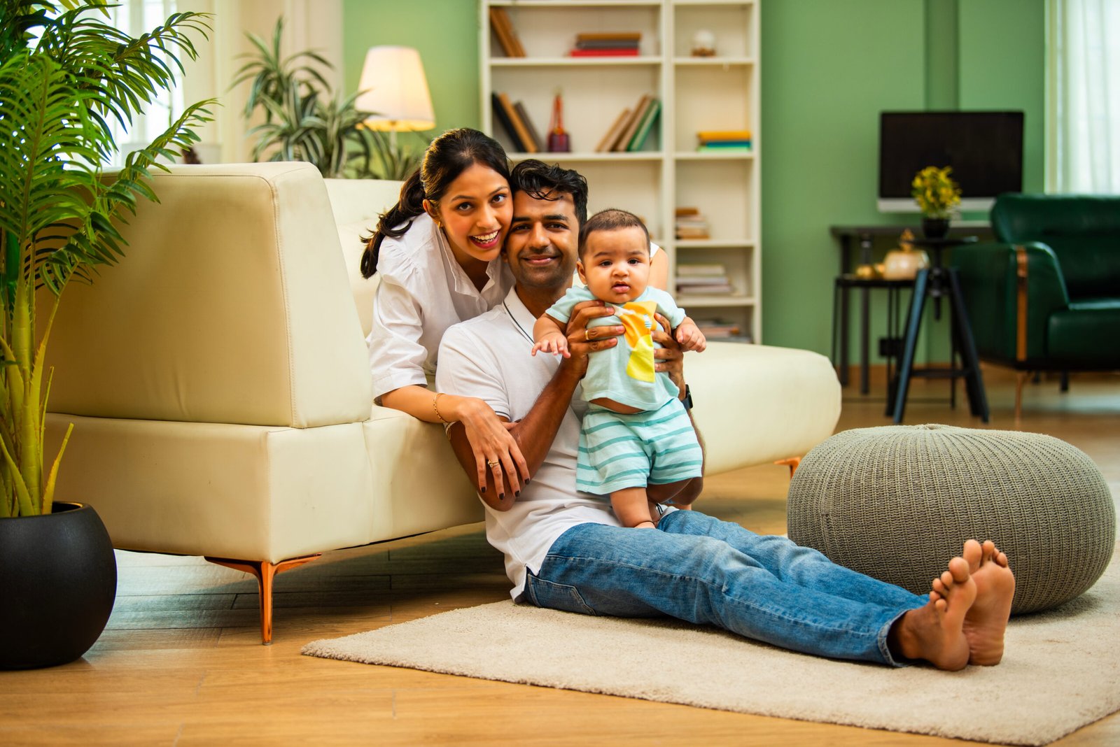 Parents sitting with baby boy while sitting on floor near sofa in modern living room, showcasing Indian family bonding, love, parenting, parenthood, emotional care, happy lifestyle, and cozy moments