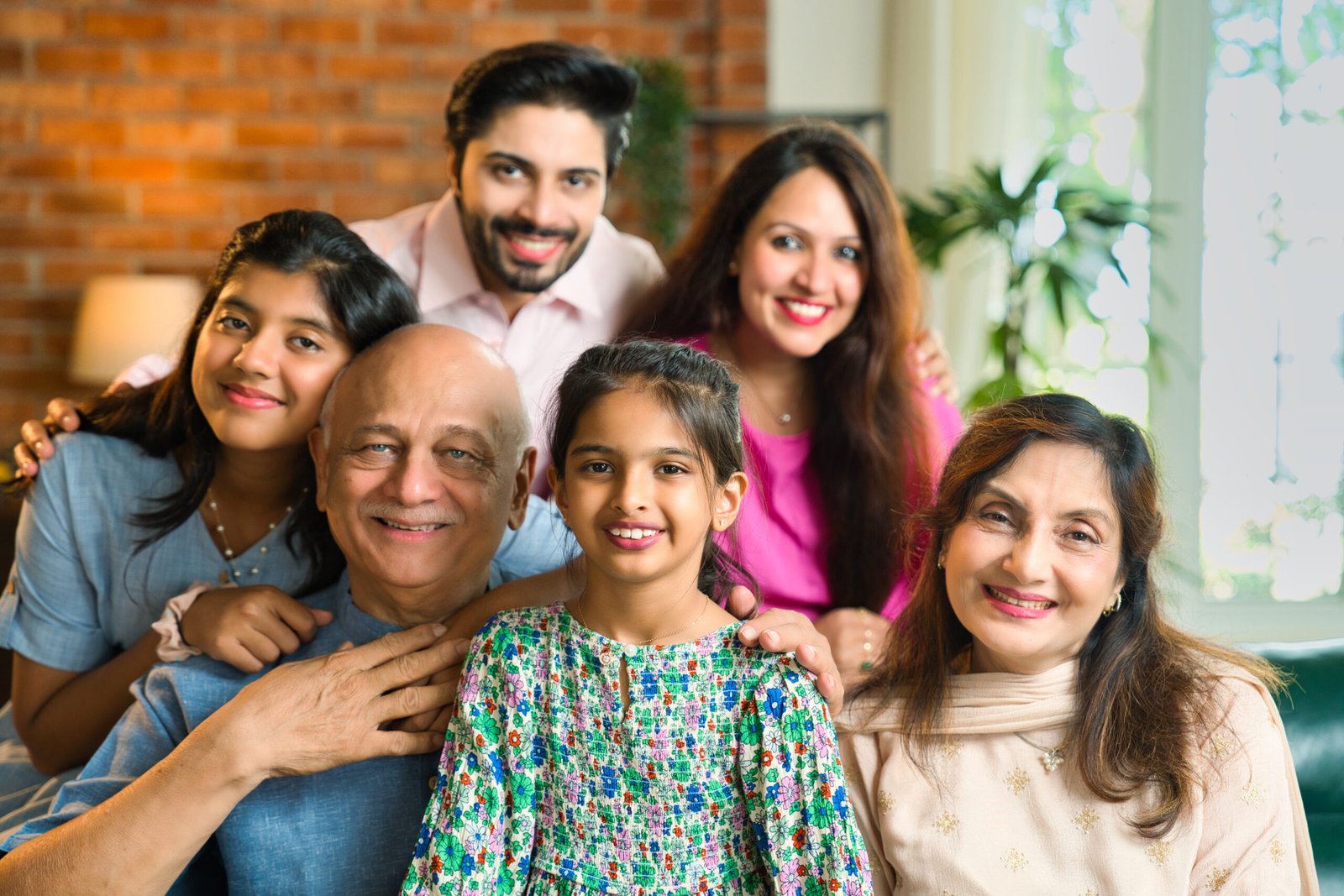 Closeup of Indian Asian multigenerational family of six sitting together on a sofa in a luxurious home, sharing happy moments and bonding across generations