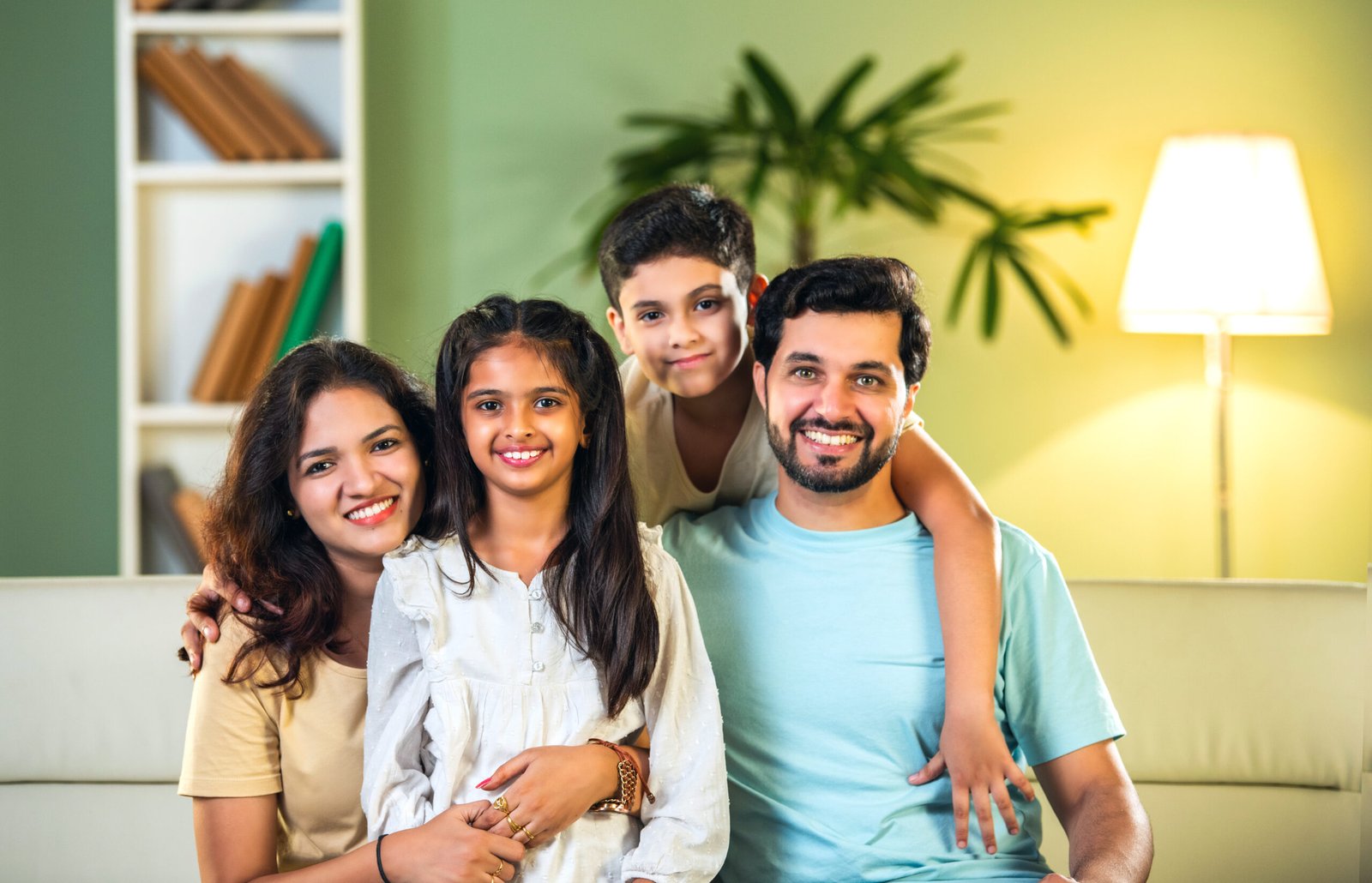 Joyful Indian family of four enjoying quality time at home, parents and kids sitting on the sofa, laughing and playing together, capturing happy moments of family bonding and love